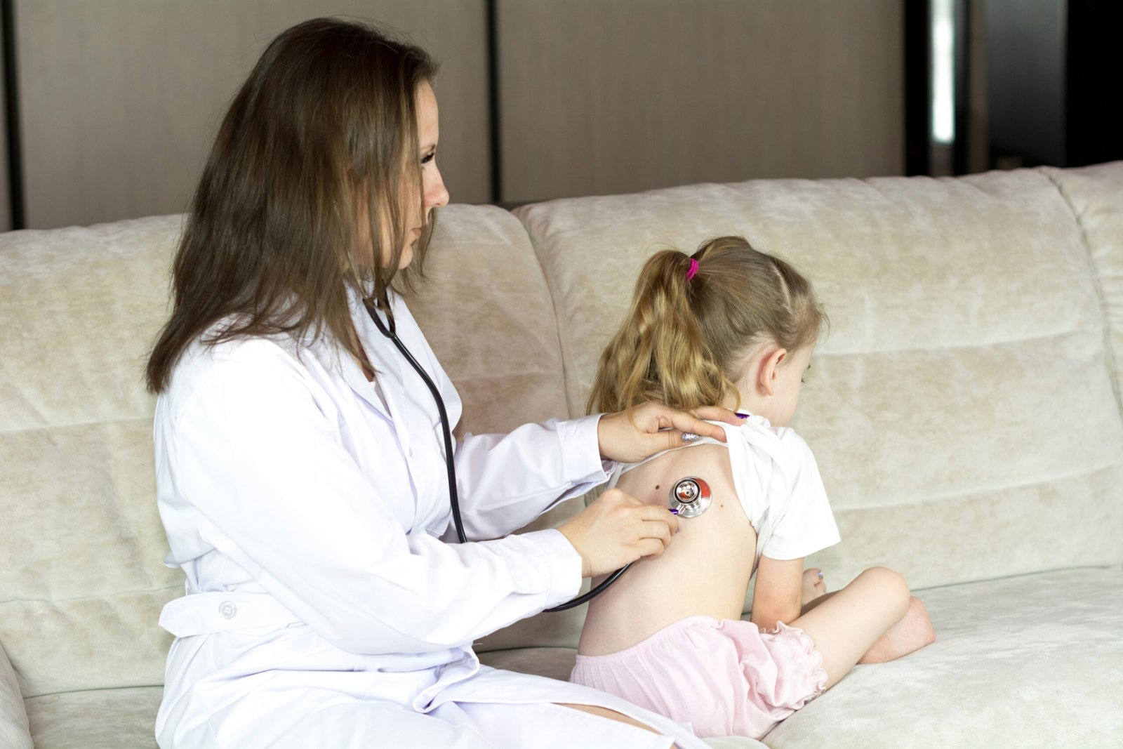 a woman in a white lab coat sitting on a couch with a little girl