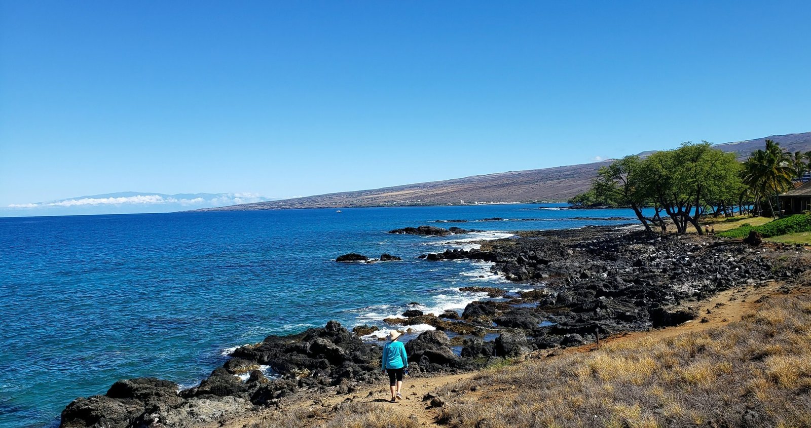 person in blue jacket standing on rock formation near body of water during daytime